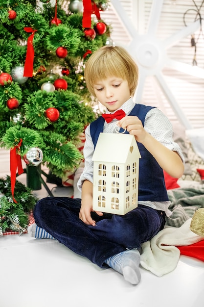 El niño se sienta en el árbol de navidad y juega