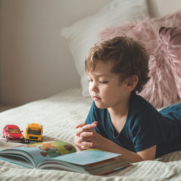 Un niño se sienta en una cama con un libro.