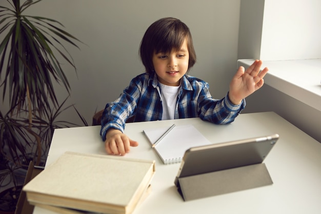 Foto el niño se sienta en un escritorio y aprende con un libro y un cuaderno de tableta