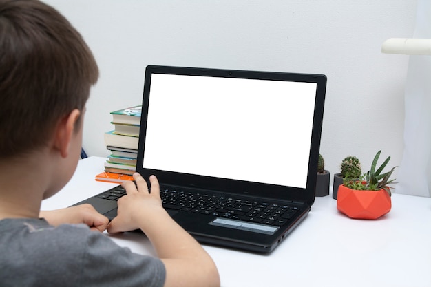 Un niño se sienta en un escritorio con una computadora portátil. Concepto de aprendizaje en casa en línea.