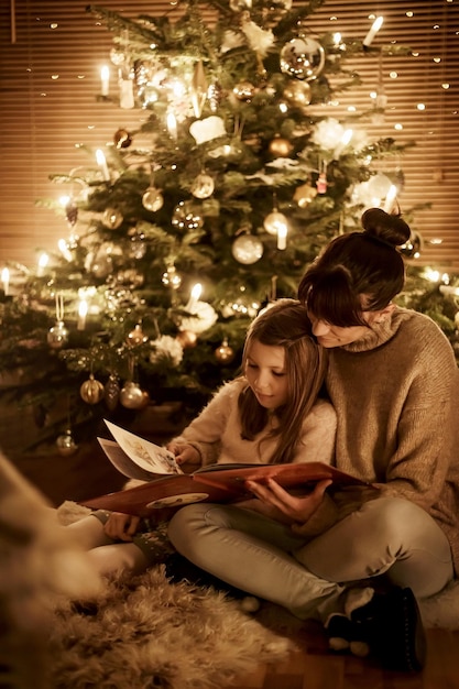 El niño se sienta con la madre frente al árbol de Navidad y leen juntos y esperan con ansias la Navidad