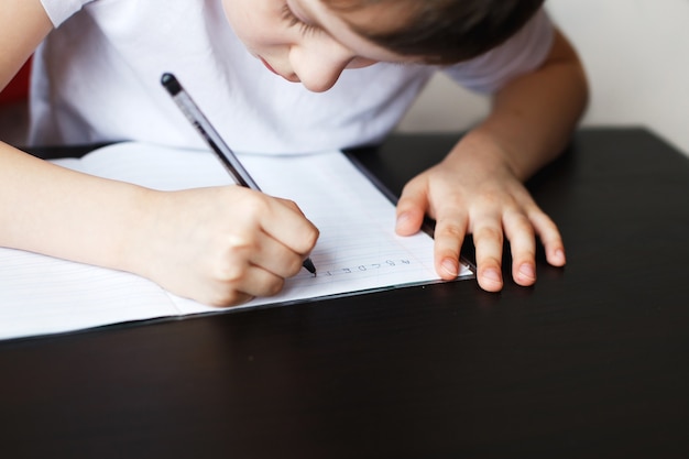 El niño se sienta a la mesa y escribe en un cuaderno.