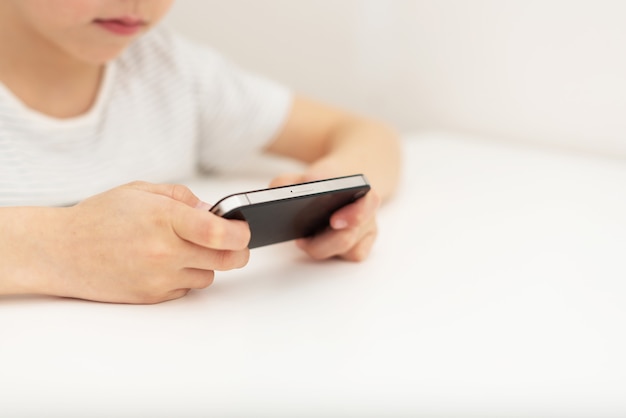 Un niño se sienta en una mesa y juega con el teléfono.