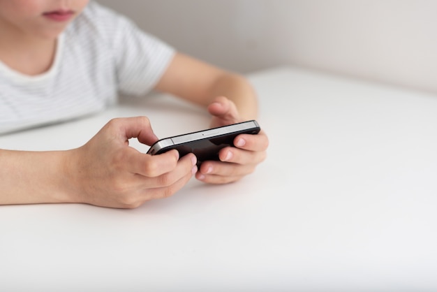 Un niño se sienta en una mesa y juega con el teléfono.