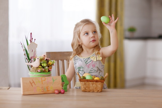 El niño se sienta a la mesa navideña con una canasta de huevos de Pascua. Sostiene un huevo en la mano y lo considera.