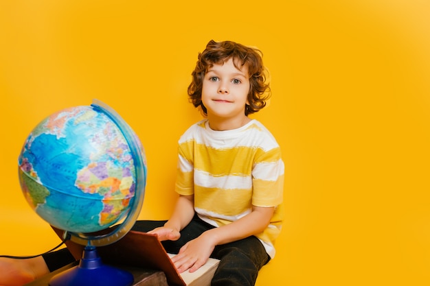 niño se sienta en una pila de libros, cerca del globo