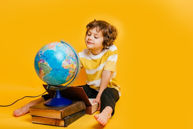 niño se sienta en una pila de libros, cerca del globo