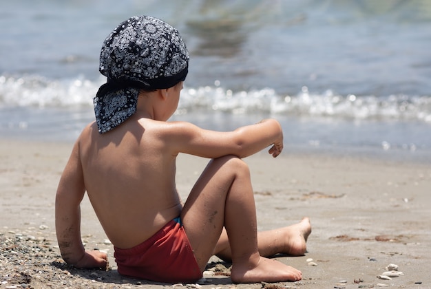 Un niño se sienta por primera vez en la orilla del mar disfrutando del aire fresco y las olas del mar.