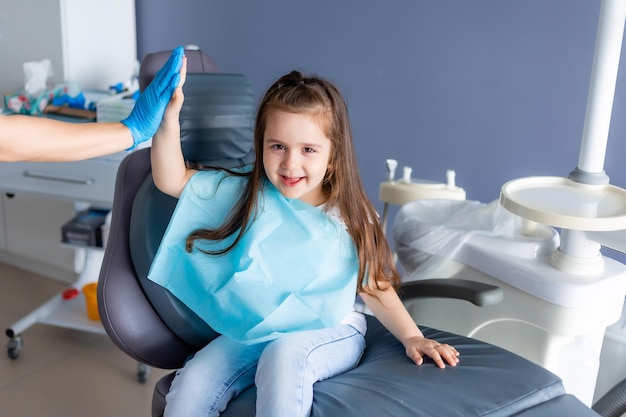 Un niño se sienta en una silla de dentista con un dentista al fondo.