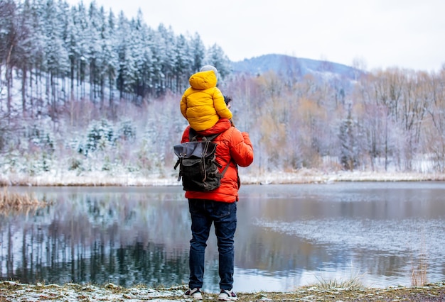 El niño se sienta sobre los hombros de su padre durante un paseo por un lago congelado en el bosque