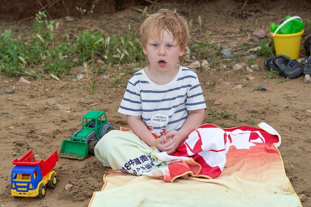 Un niño se sienta en una toalla en una playa de arena entre juguetes