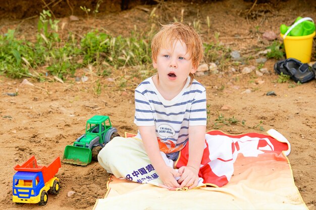 Un niño se sienta en una toalla en una playa de arena entre juguetes