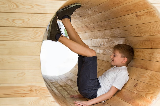 El niño se sienta en un túnel de madera Parque infantil ecológico