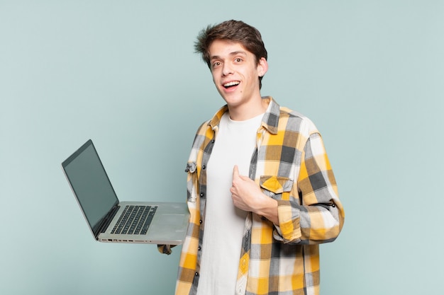 El niño se siente feliz, sorprendido y orgulloso, señalando a sí mismo con una mirada emocionada y asombrada. concepto de laptop
