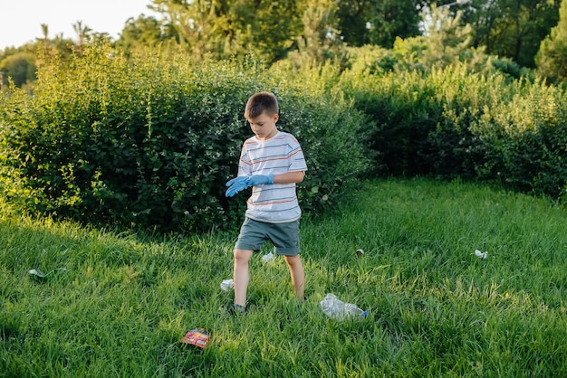 Un niño de siete años al atardecer se dedica a la recolección de basura en el parque. Cuidado del medio ambiente, reciclaje.