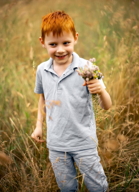 Un niño de siete años con cabello rojo con un ramo de flores silvestres en verano.