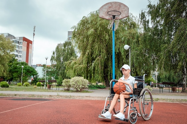 Niño en silla de ruedas en la cancha de baloncesto. Rehabilitación, persona discapacitada, paralizada, feliz niño discapacitado.