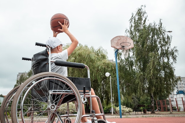 Niño en silla de ruedas en la cancha de baloncesto. Rehabilitación, persona discapacitada, paralizada, feliz niño discapacitado.