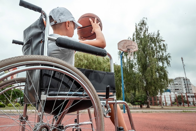 Niño en silla de ruedas en la cancha de baloncesto. Rehabilitación, persona discapacitada, paralizada, feliz niño discapacitado.