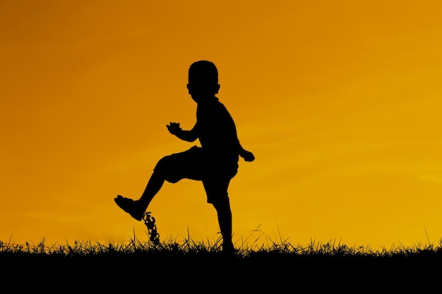 Foto niño silueta jugando contra el cielo durante la puesta del sol
