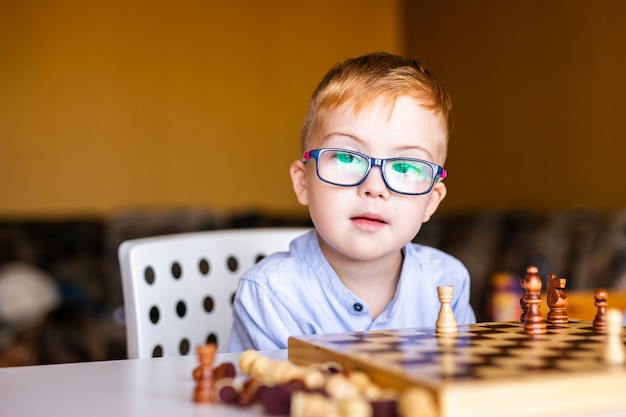 Niño con síndrome de down con gafas grandes jugando al ajedrez