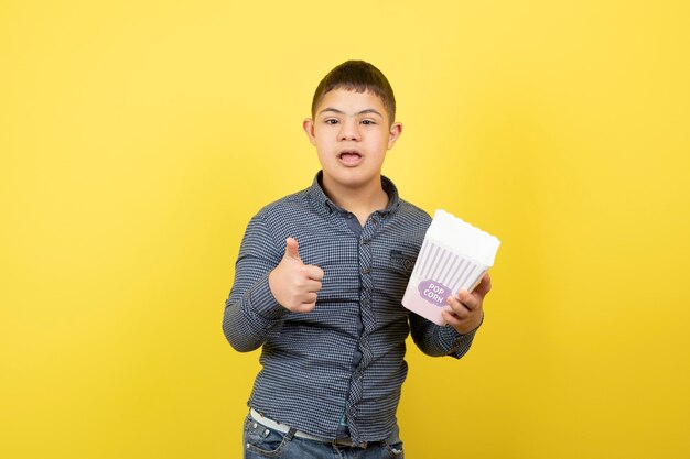 Niño con síndrome de down sosteniendo una caja de palomitas de maíz y dando pulgares hacia arriba.