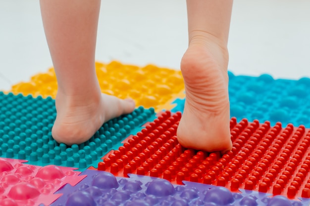 Niño sobre colchoneta de masaje para pies de bebé. Ejercicios para piernas sobre alfombra de masaje ortopédico. prevención de pies planos y hallux valgus