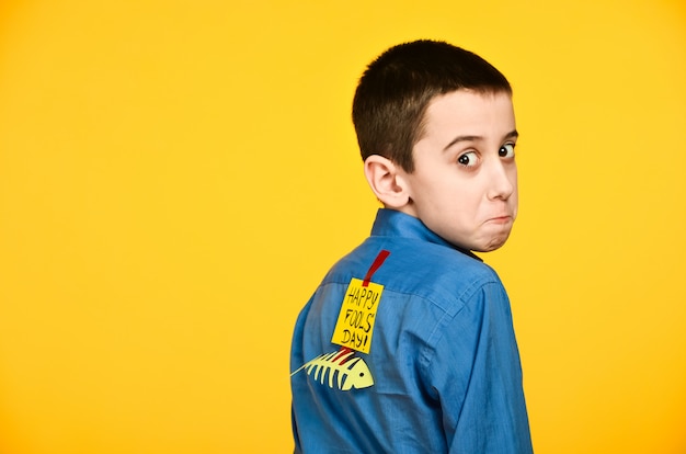 El niño sobre un fondo amarillo con una camisa azul con una cinta adhesiva de pescado y un trozo de papel en la espalda