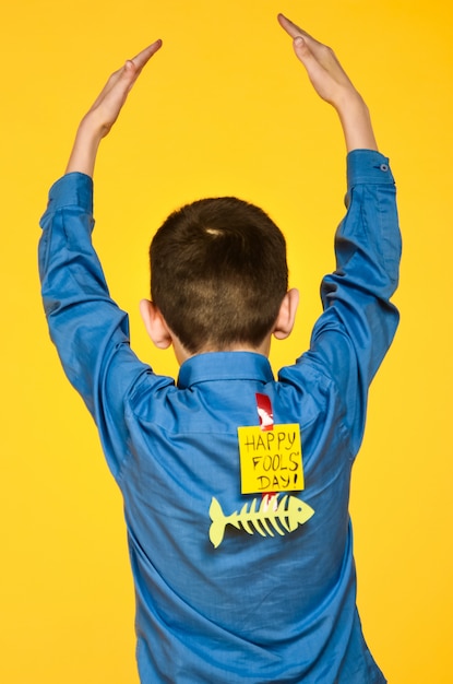 Foto el niño sobre un fondo amarillo con una camisa azul con una cinta adhesiva de pescado y un trozo de papel en la espalda