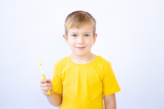 Un niño sobre un fondo blanco se está cepillando los dientes sosteniendo un cepillo de dientes en sus manos aislar