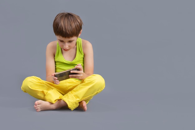 Niño sobre un fondo gris con un teléfono móvil El niño juega en el teléfono inteligente