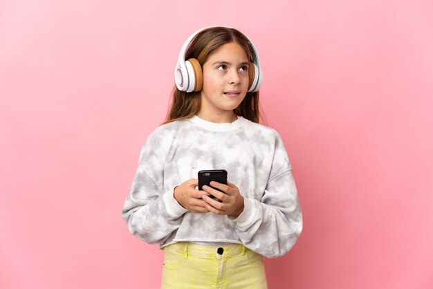 Niño sobre fondo rosa aislado escuchando música con un móvil y pensando