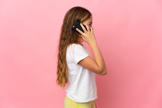 Niño sobre fondo rosa aislado manteniendo una conversación con el teléfono móvil con alguien