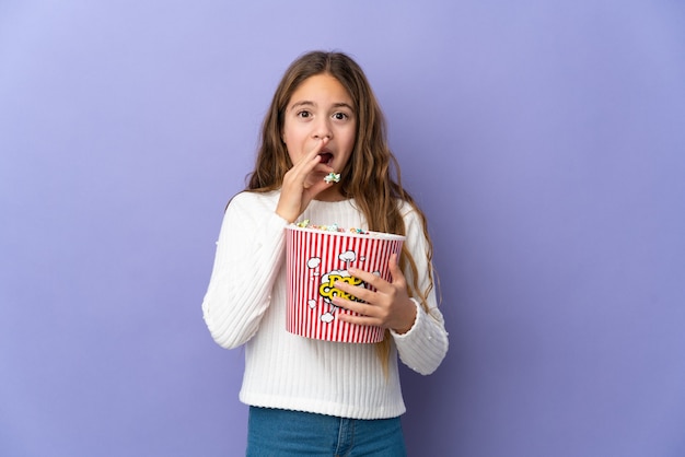 Niño sobre pared púrpura aislada sosteniendo un gran balde de palomitas de maíz