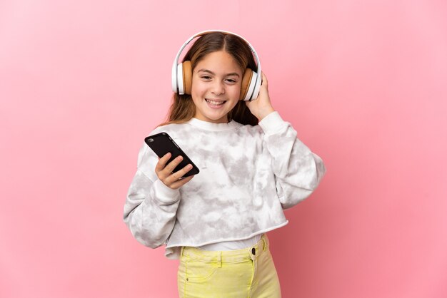 Niño sobre pared rosa aislada escuchando música con un móvil y cantando