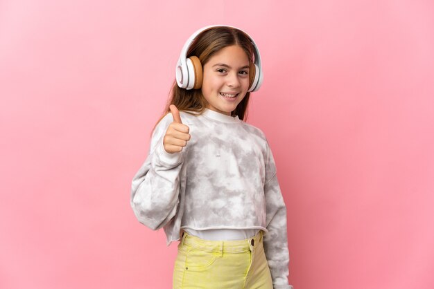 Niño sobre pared rosa aislada escuchando música y con el pulgar hacia arriba