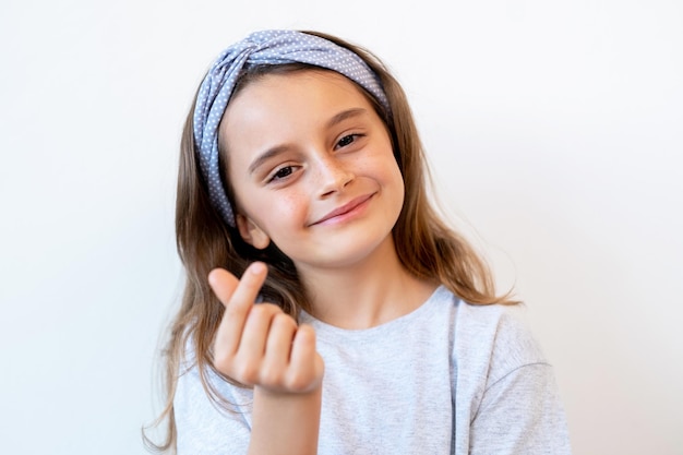 Niño solidario. Signo de amor. Afecto amistad. Retrato de una niña pequeña sonriente alegre y alegre que muestra un gesto de corazón con el dedo aislado en el fondo blanco.