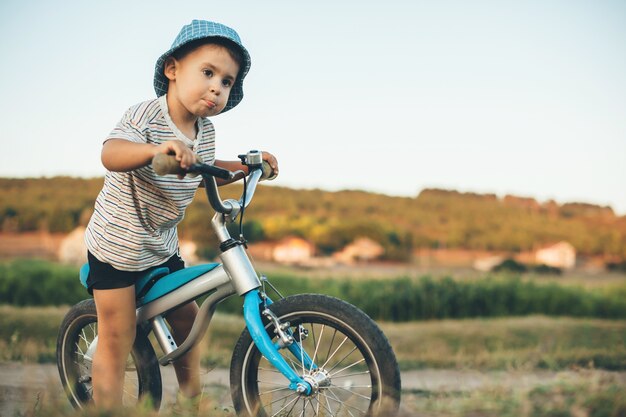 Niño con sombrero azul y bicicleta mirando en algún lugar de un campo