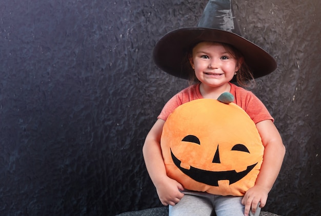 Niño con sombrero de bruja con almohada de calabaza sobre fondo negro