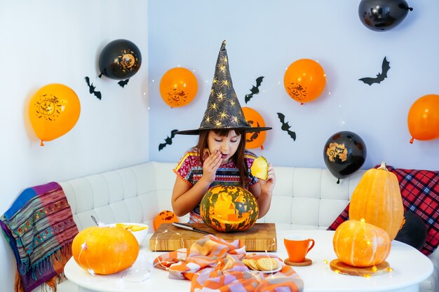 Niño con sombrero de bruja divirtiéndose mientras hace algunas calabazas de Halloween