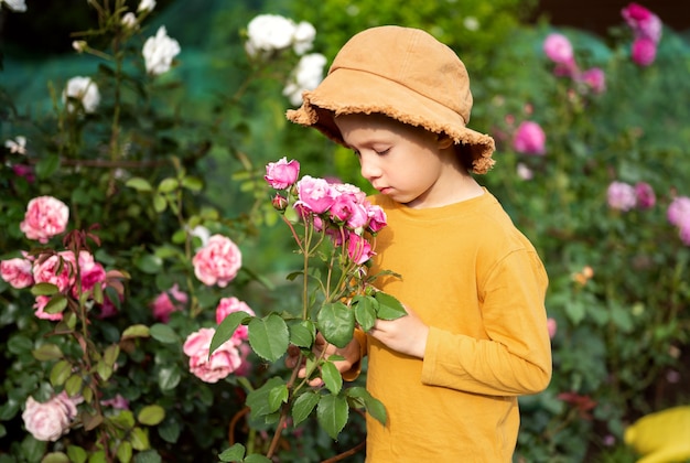 Un niño con sombrero huele rosas en el jardín.