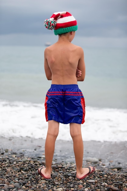 Niño con un sombrero de Navidad en la orilla de la mar Reunión de Navidad en los países del sur