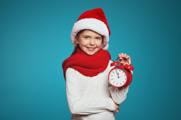 Niño con sombrero de navidad y pañuelo rojo con reloj despertador aislado sobre