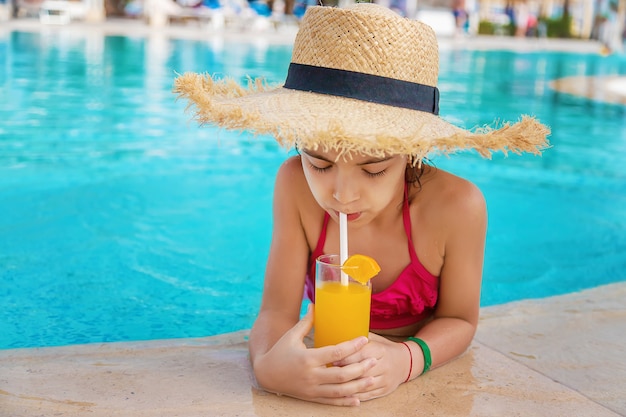 Niño con sombrero de paja bebiendo un cóctel junto a la piscina