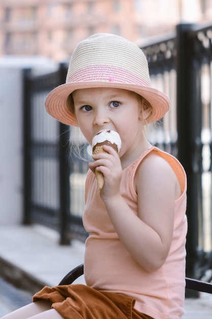 Un niño con un sombrero de paja se sienta en un banco. Una niña está comiendo helado.