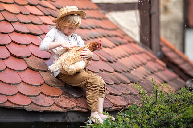 Un niño con un sombrero de paja se sienta en el techo con su pájaro favorito.