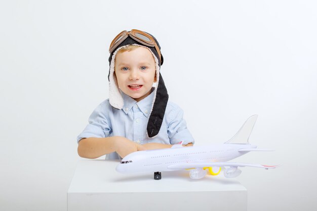 Niño con sombrero de piloto y con un avión sobre un fondo blanco.