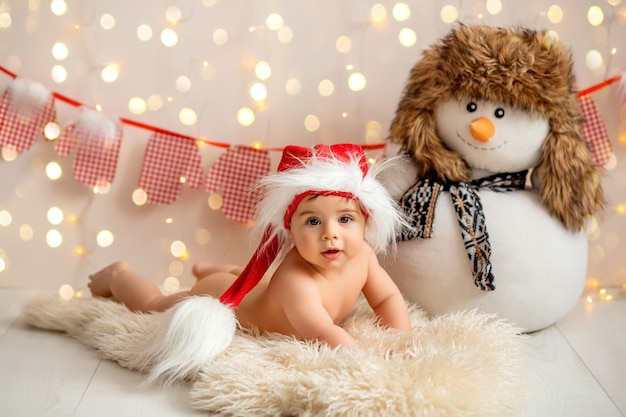 Un niño con un sombrero de Santa Claus con un muñeco de nieve en el fondo de luces borrosas