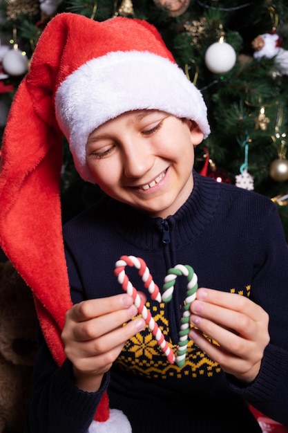 Niño sombrero Santa Claus sonriendo y sosteniendo un bastón de piruleta de caramelo