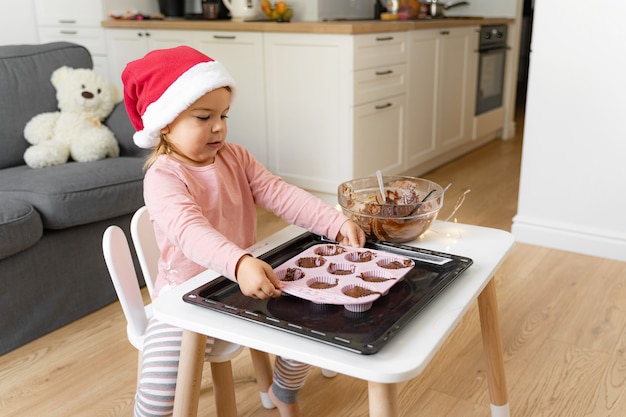 Niño con sombrero de santa preparando galletas navideñas en casa. Actividad navideña en casa para niños pequeños